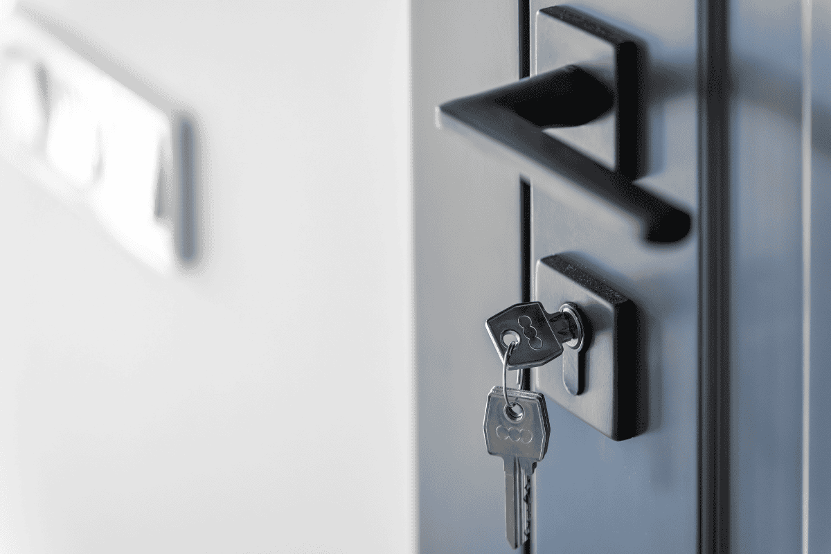 Close-up of keys in a door lock on a dark blue metal door, with a lever handle nearby